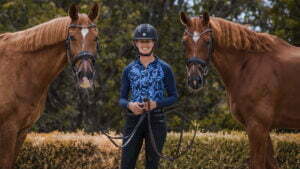A person wearing a helmet and blue patterned shirt stands outdoors holding the reins of two brown horses, one on each side, with trees and bushes in the background—like a perfect image for a Sales Page Template.