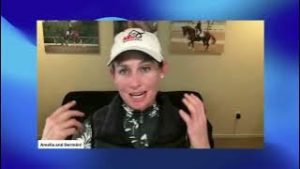 A person wearing a white cap and patterned shirt gestures while speaking on a video call, with horse show photos on the wall behind them. A text label in the lower left corner reads Amelia and German.