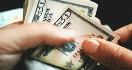 A close-up of hands flipping through a stack of U.S. fifty-dollar bills, counting the money—much like tallying up Rider Standings in 2023.
