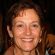 A middle-aged woman with short brown hair, wearing earrings and a brown jacket, smiles warmly at the camera. Set against a dark, blurred background, her confident expression could grace a 2024 Sale Page or Training Scale guide.